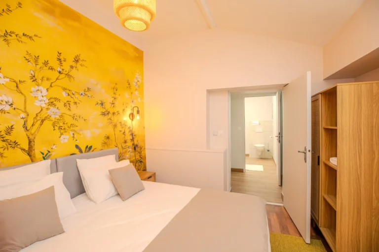 Chambre avec lit double et mur décoré d'une fresque florale jaune, vue sur la salle de bain