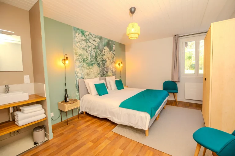 Chambre avec lit double, murs verts pastel, déco florale et accents turquoise, avec coin lavabo