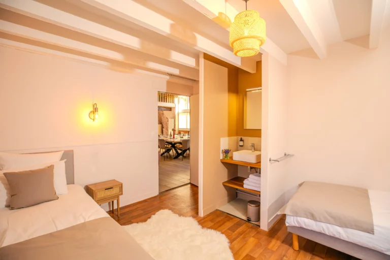 Chambre avec deux lits simples, coin lavabo et vue sur la salle à manger