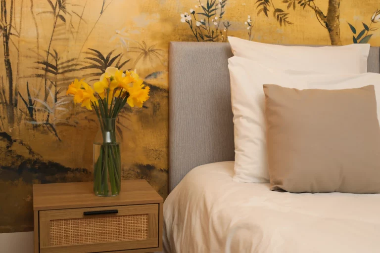 Table de chevet en bois avec vase de jonquilles jaunes à côté d’un lit