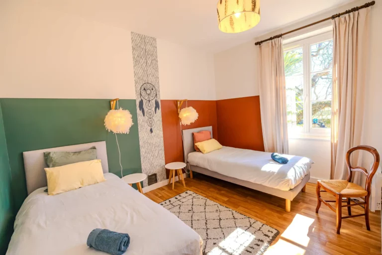 Chambre avec deux lits simples colorés, décorée dans un style moderne et chaleureux avec capteur de rêves mural