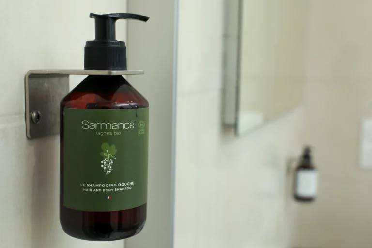 Flacon mural de shampoing douche bio Sarmance fixé sur un mur carrelé, reflet visible dans un miroir de salle de bain